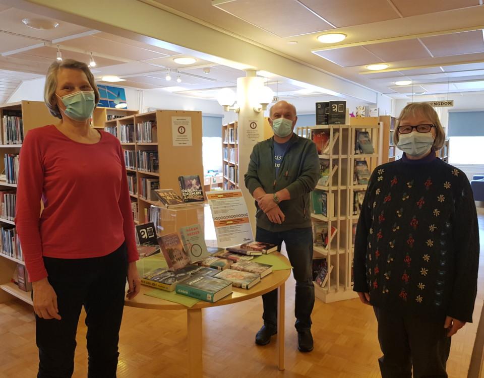 Tre personer med munskydd i ett bibliotek