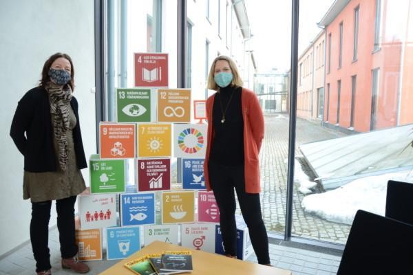 två kvinnor står framför stora pusselbitar som berättar om agenda 2030-mål, texter om en hållbar natur