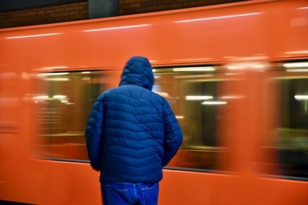 en person med blå jacka står vid en orange metro som rör sig snabbt