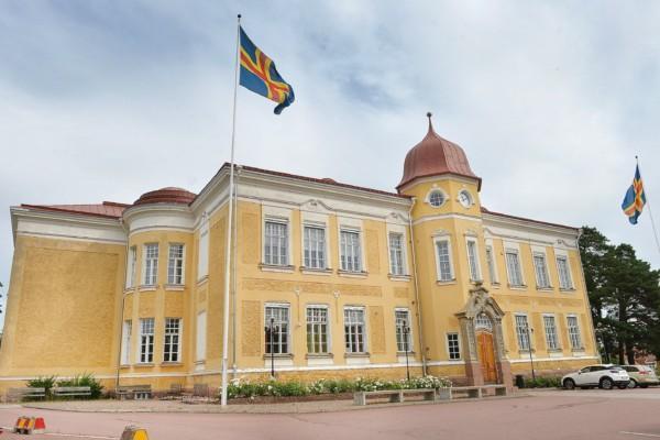 en gul stenbyggnad med åländska flaggan vajande framför