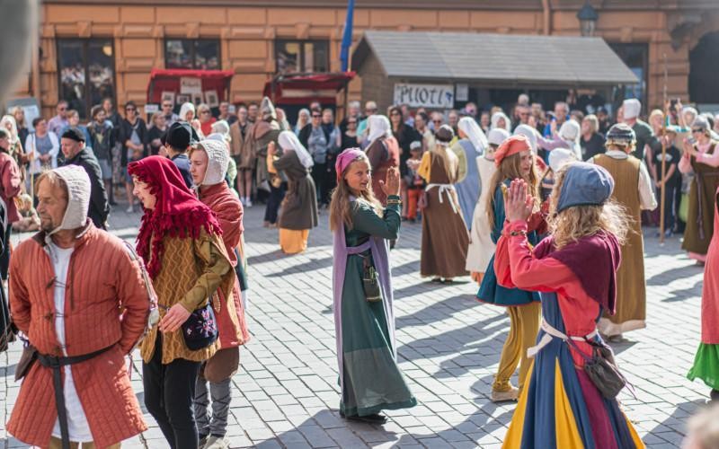 folksamling klädda i medeltidsutstyrsel dansar på torg