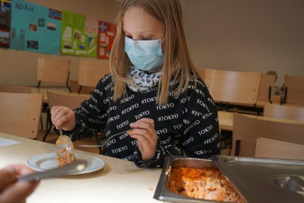 en flicka med munskydd lägger upp mat på sin tallrik