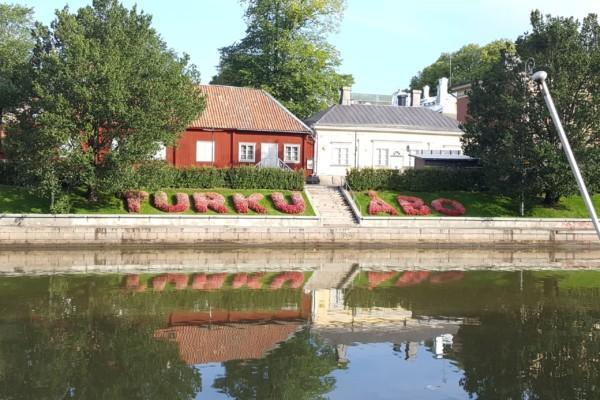 Aura å i Åbo och hus som speglar sig i vatten och blommor som bildar ordet Åbo