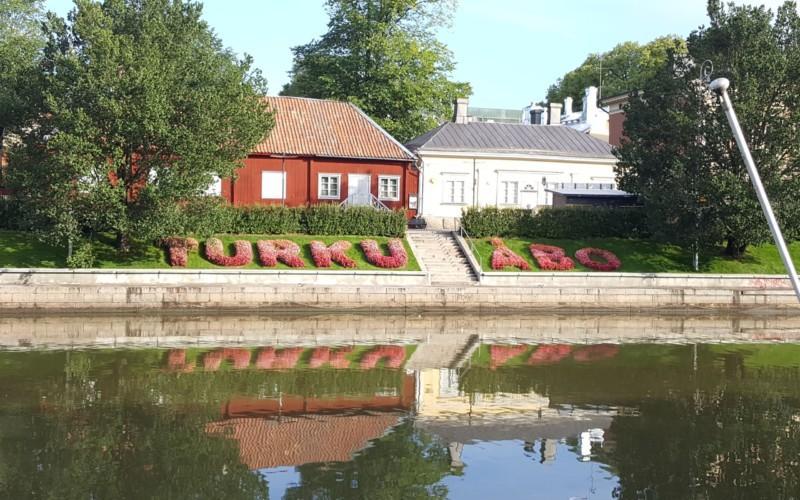 Aura å i Åbo och hus som speglar sig i vatten och blommor som bildar ordet Åbo