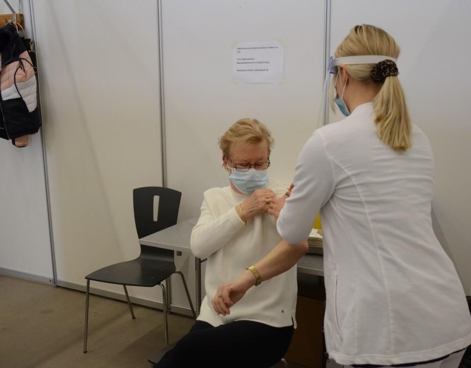 kvinna sitter på en stol och sköterska putsar hennes arm för vaccin