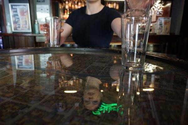 en kvinna tömmer ett bord på tomma ölstop, hennes ansikte reflekteras i glasbordet