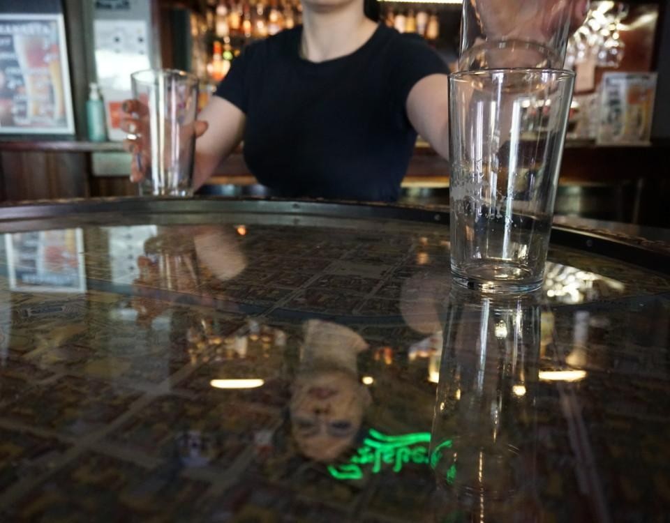 en kvinna tömmer ett bord på tomma ölstop, hennes ansikte reflekteras i glasbordet