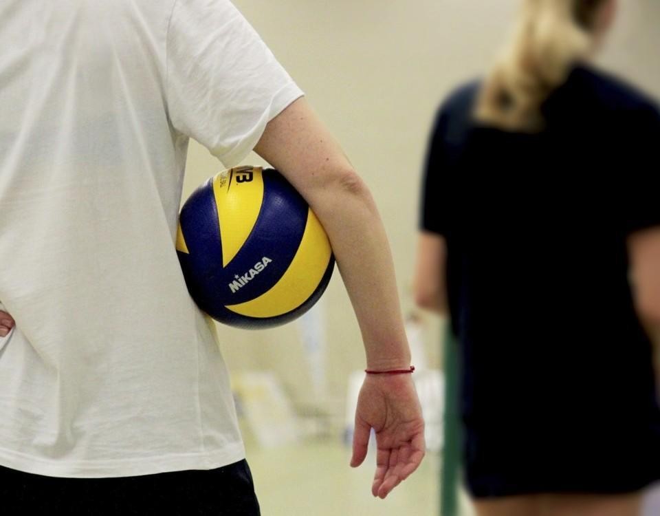 en ung person står med en volleyboll under armen