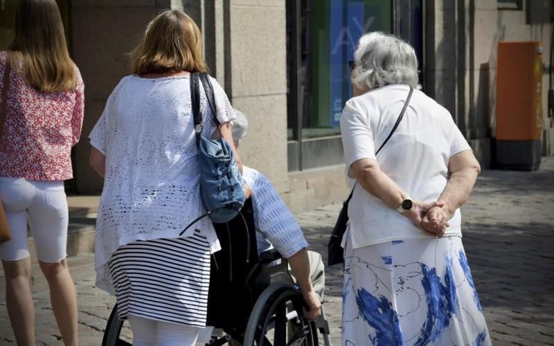 en kvinna skuffar en äldre kvinna i rullstol, en annan kvinna går bredvid