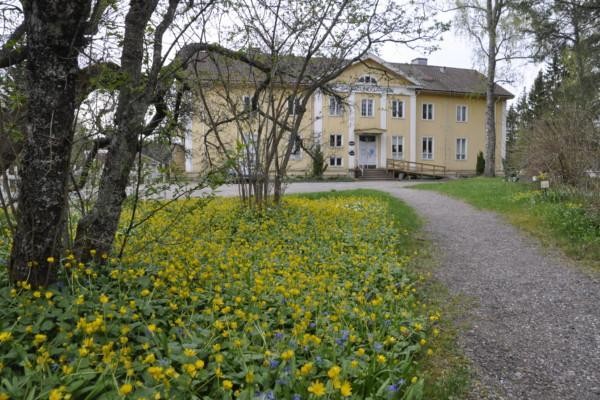 Stor gul byggnad i bakgrunden. I förgrunden gula blommor