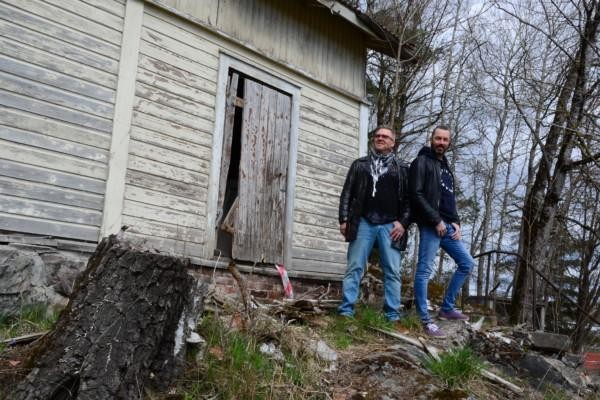 två män poserar framför ett fallfärdigt hus