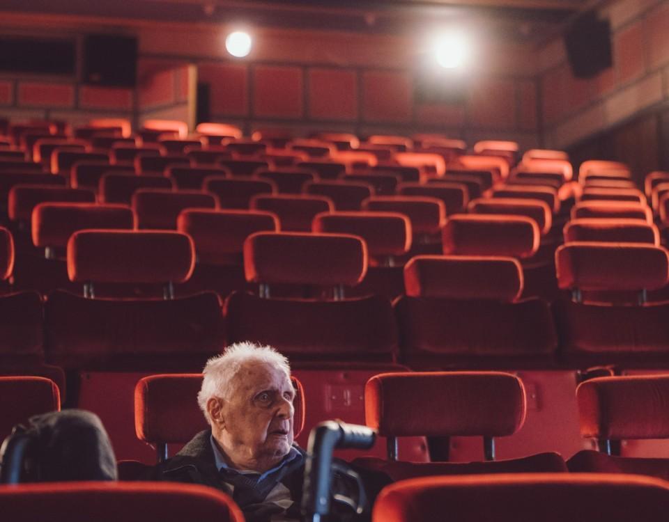 en gammal man sitter ensam i en stor biosalong