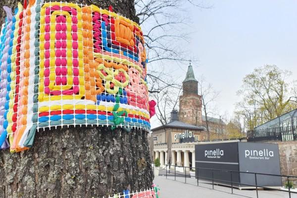 ett stickat och färggrannt konstverk klär ett träd i stan