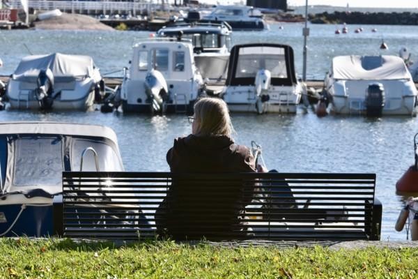 En person sitter på en bänk och blickar ut över en båthamn.