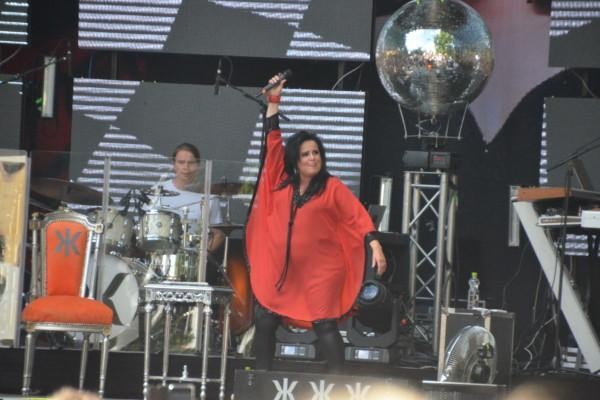 En kvinna iklädd röda kläder står på en scen och håller mikrofonen upp i luften.