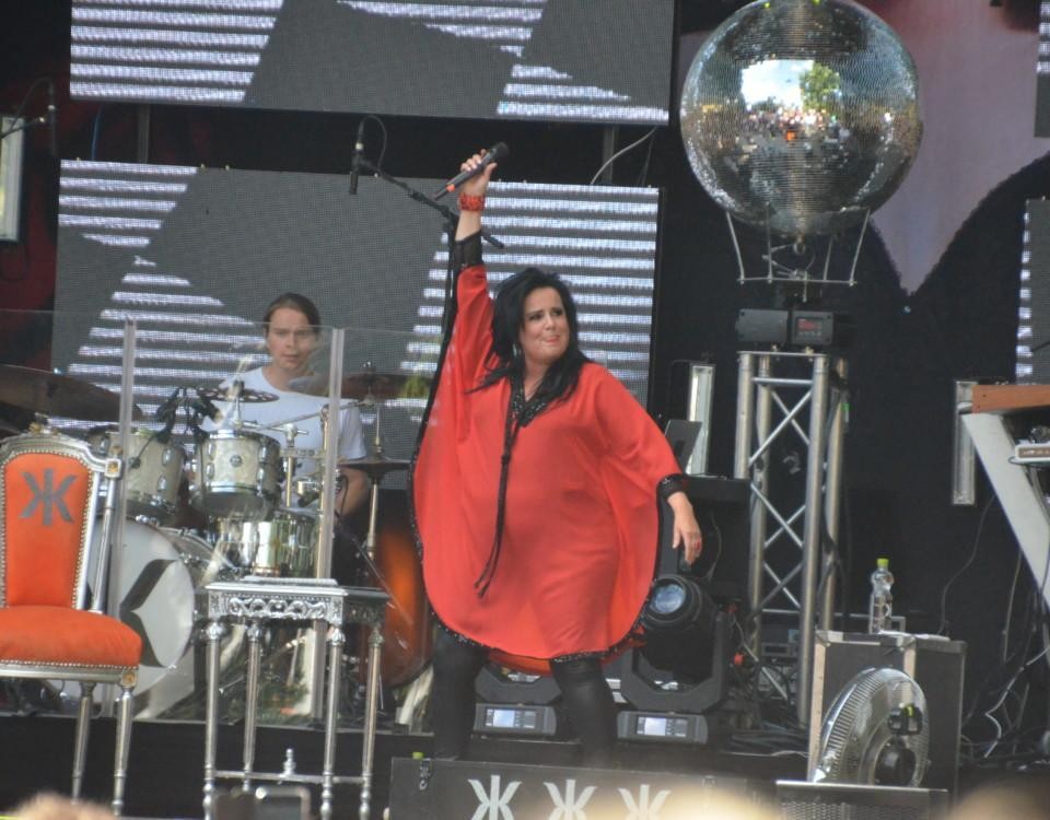 En kvinna iklädd röda kläder står på en scen och håller mikrofonen upp i luften.