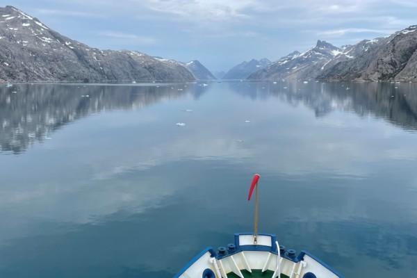 Fören på en båt som färdas i en fjord. Havsytan är glasblank.