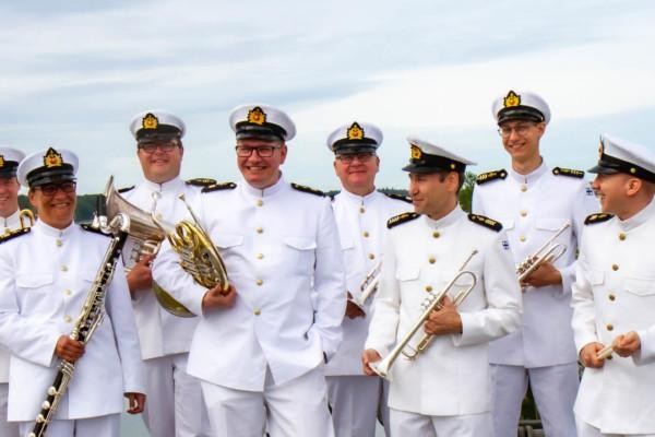 En rad med män iklädda flottans vita uniformer håller i olika blåsinstrument.