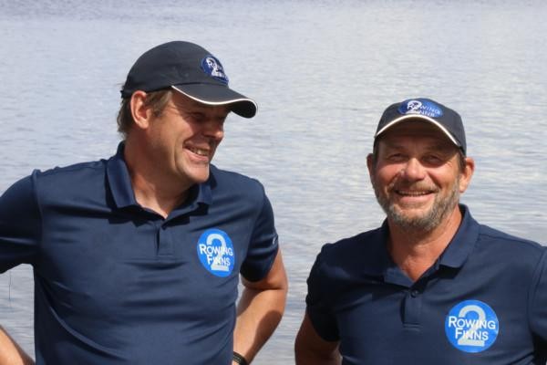 Två män iklädd mörkblå t-skjorta och keps skrattar i bakgrunden syns endast vatten
