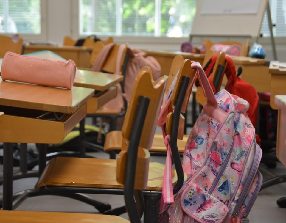 Skolväskor som hänger på stolar i ett klassrum.