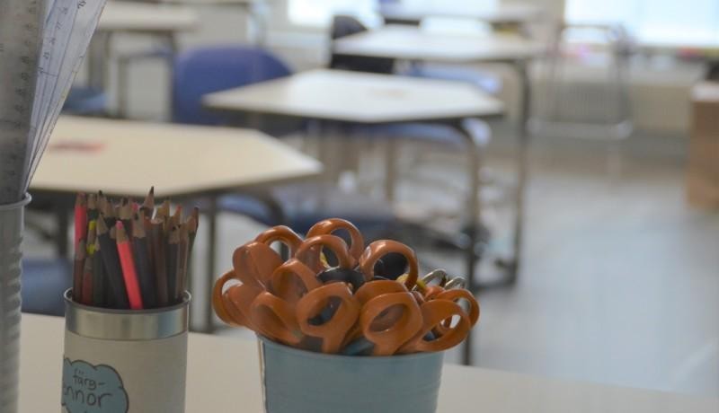 En kopp med pennor och saxar, suddigt i bakgrunden syns pulpeter