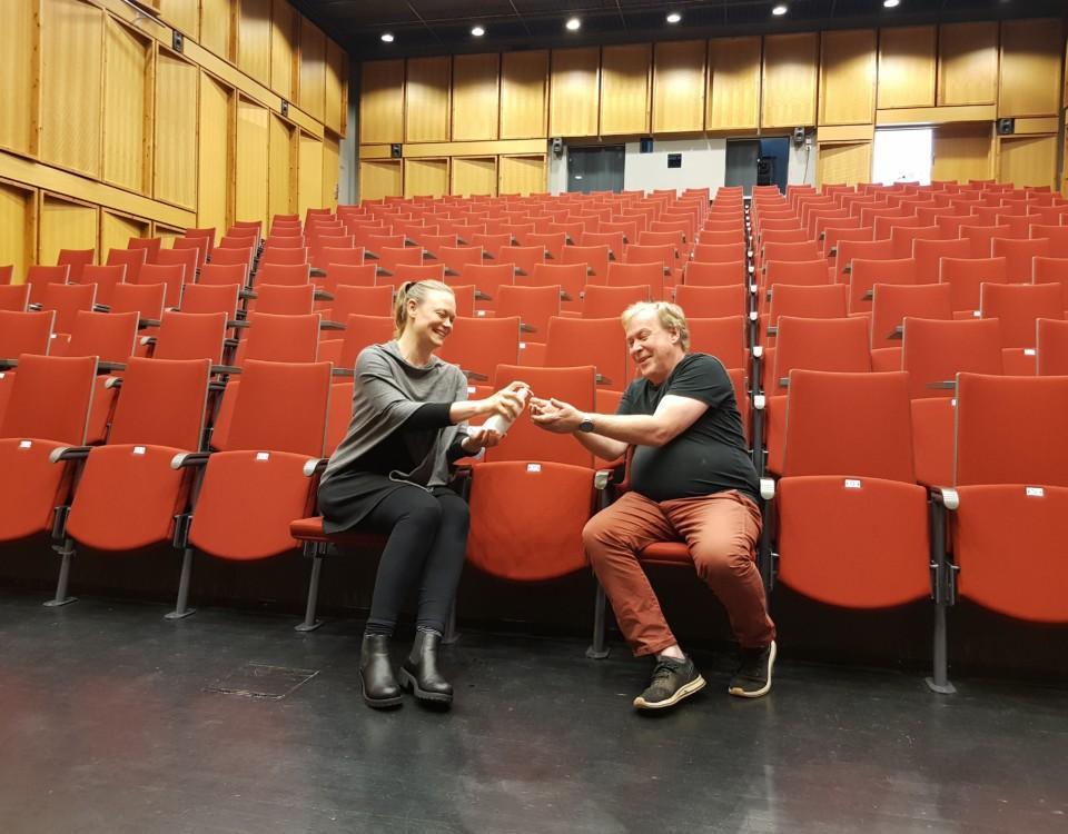 Man och kvinna använder handsprit i ett stort auditorium