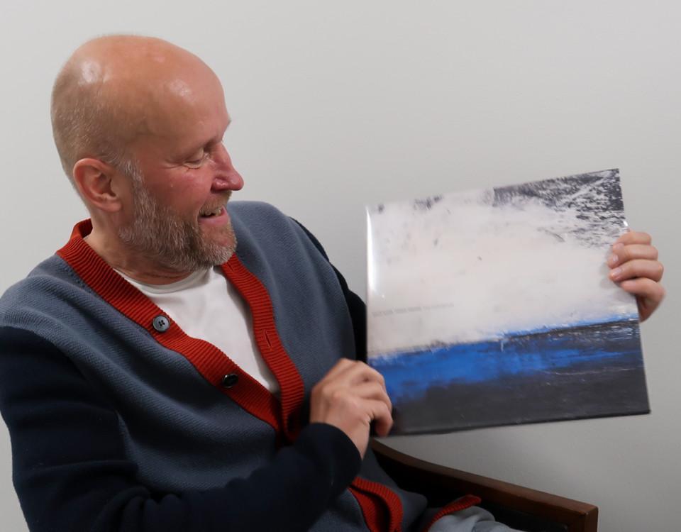 Porträtt av man som sitter och håller upp en vinylalbum som han tittar på. Albumets omslag föreställer en målning av ett hav.