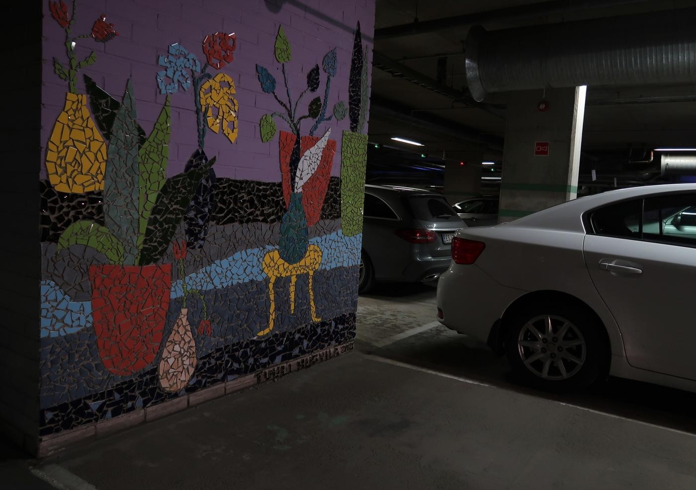 Bild av en bil i en parkeringshall so står invid en vägg som är prydd med mosaikkonst.