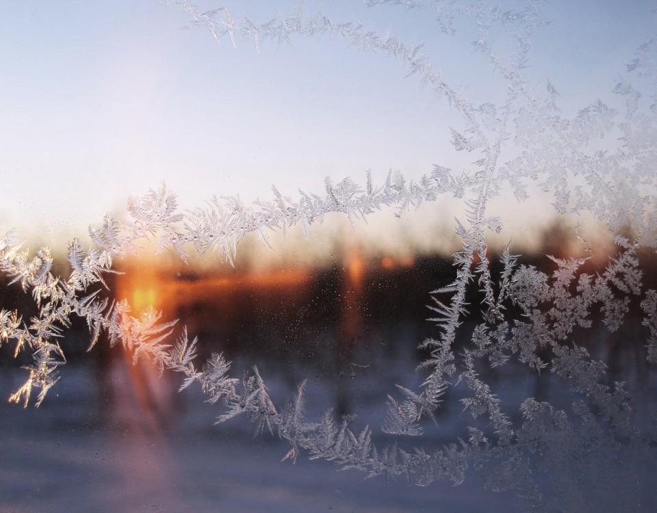Frostigt fönster med solnedgång över snö i bakgrunden.