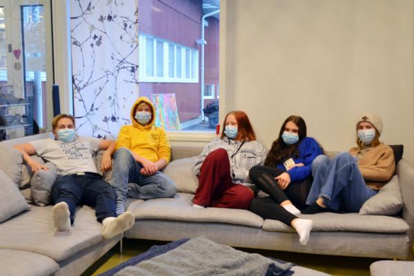 fem ungdomar med munskydd sitter i en soffa