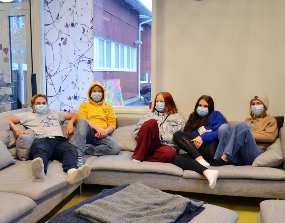 fem ungdomar med munskydd sitter i en soffa