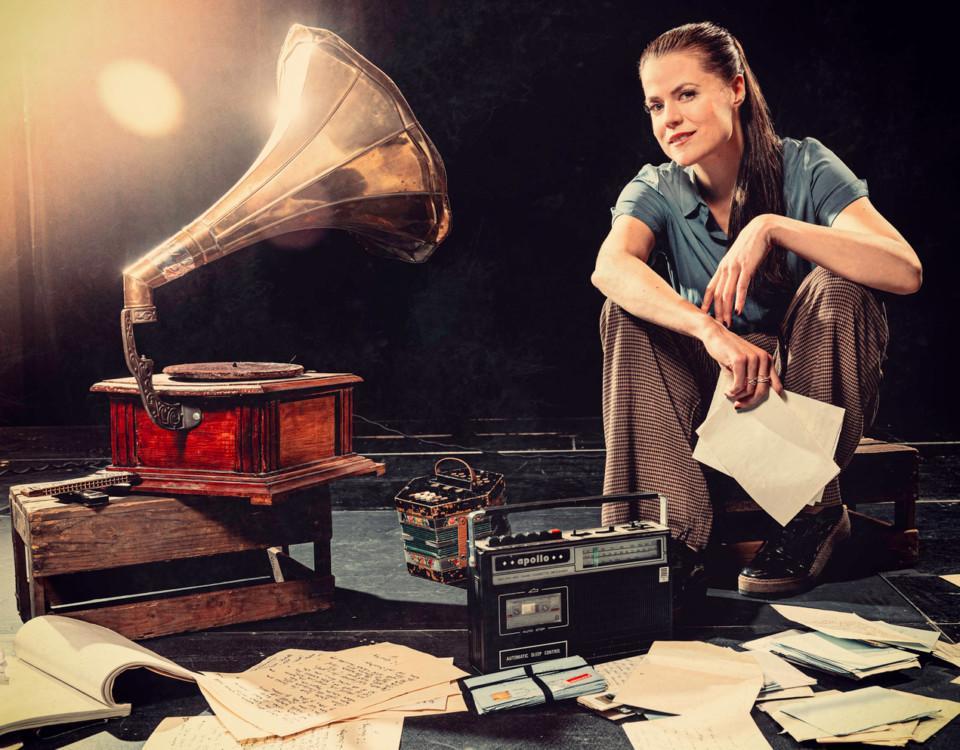 Kvinna sitter bland apparater som gammal grammofon och radio.