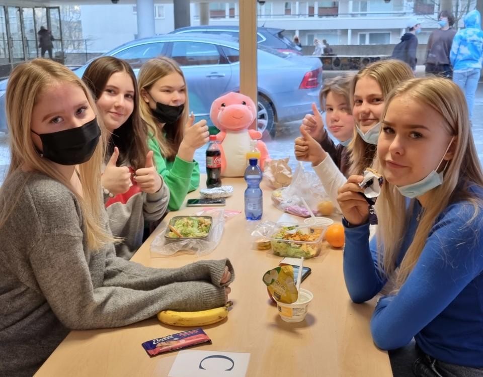 skolflickor sitter runt ett bord äter