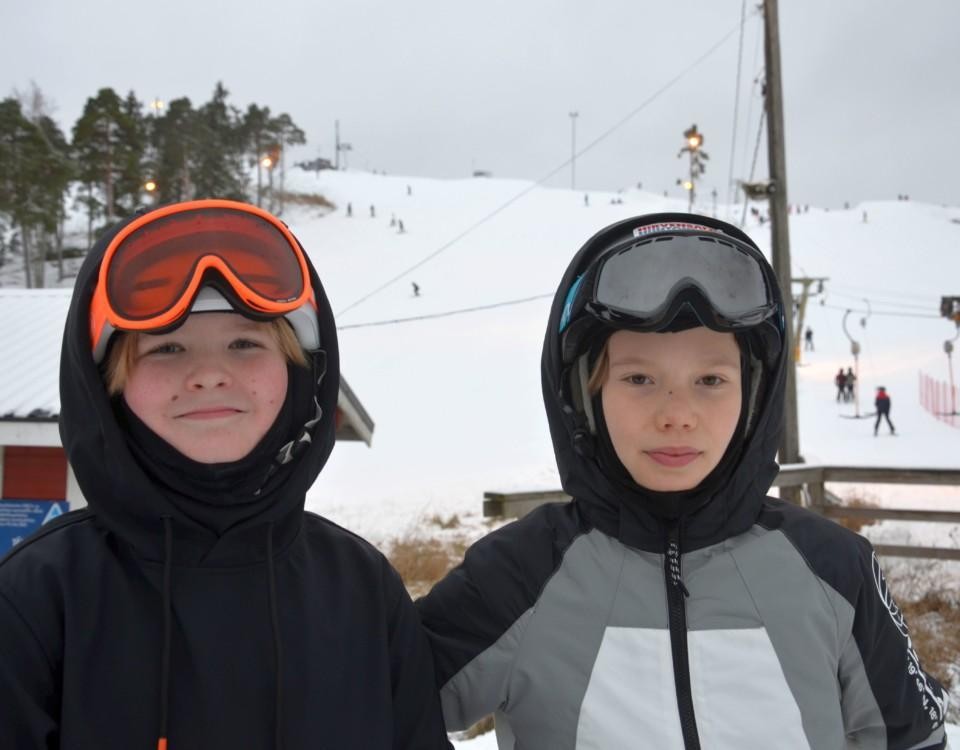Två pojkar i slalomutrustning vid skidbacke