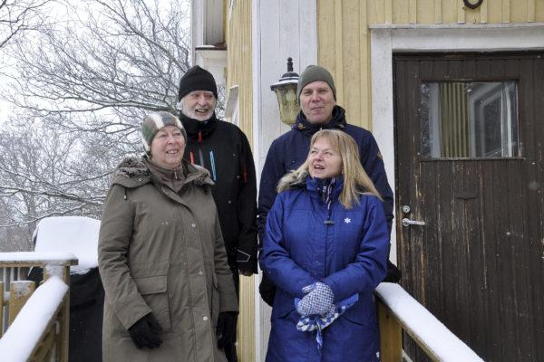 Fyra personer utomhus i vinterkläder vid ett gult hus