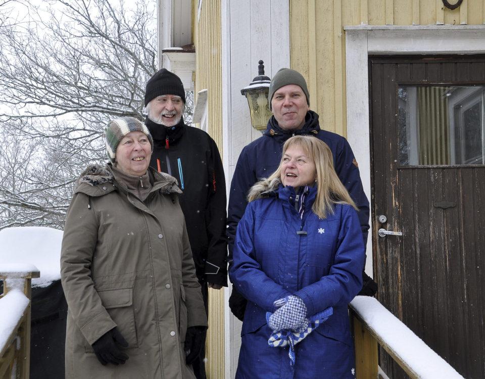 Fyra personer utomhus i vinterkläder vid ett gult hus