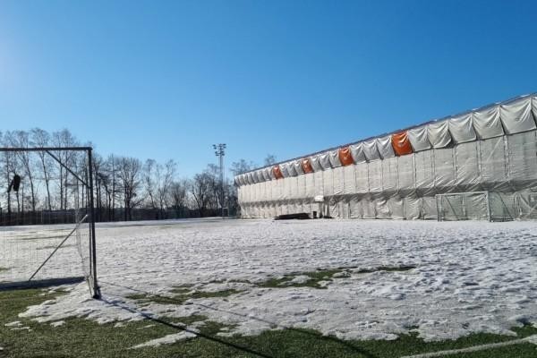 fotbollsplan med snö och inpaketerad läktare i bakgrunden, blå himmel