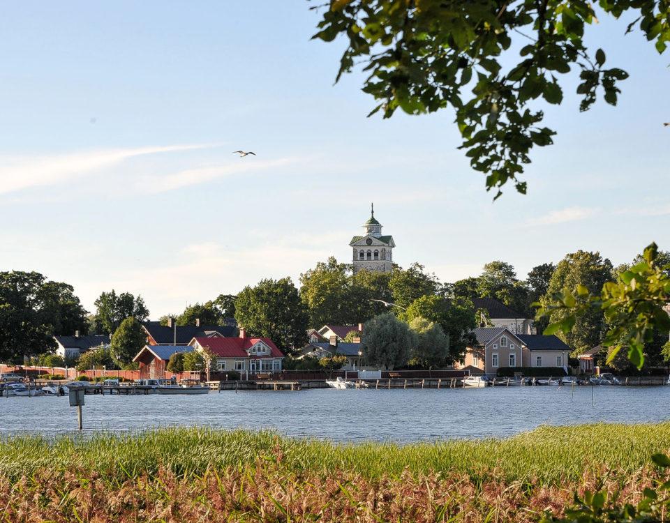 Sommar. En vik, trähus och ett kyrktorn