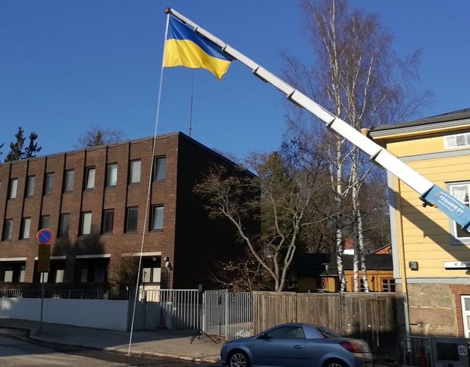 Kran lyfter flagga upp i ett träd i en park vid ett höghus