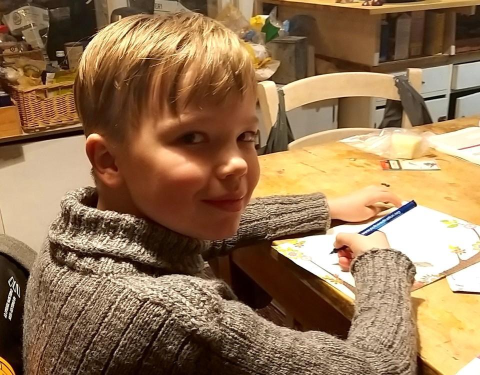 pojke skriver brev vid ett köksbord