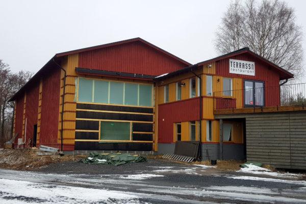 Större träbyggnad i rött och gult. Den ena sidan en säsonstängd restaurang med uteservering