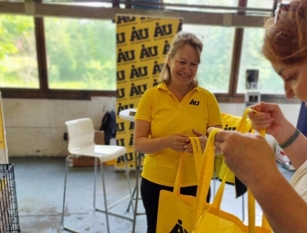 kvinna i gul pikéskjorta ger gul kasse till annan person