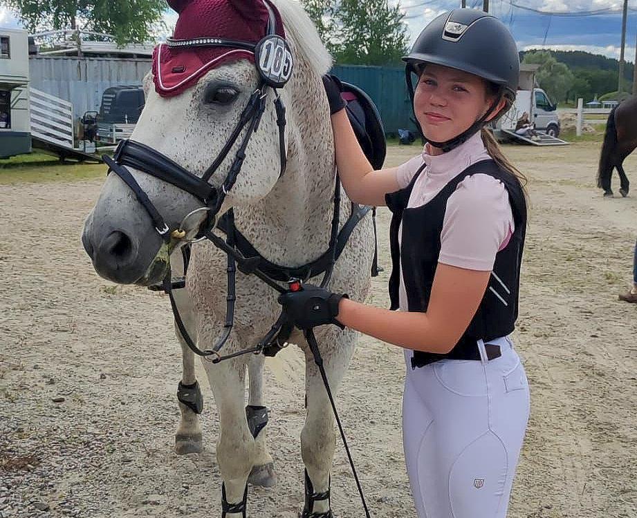 flicka står bredvid en ljus häst på en tävlingsplats