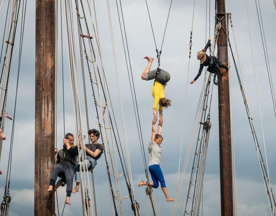 fem personer gör konster uppe i masterna på en segelskuta