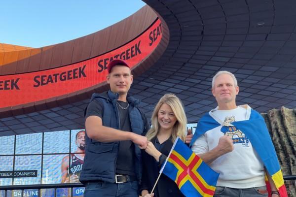 Tre personer med Ålands flagga vid en arena.
