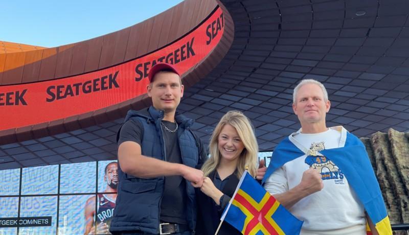 Tre personer med Ålands flagga vid en arena.