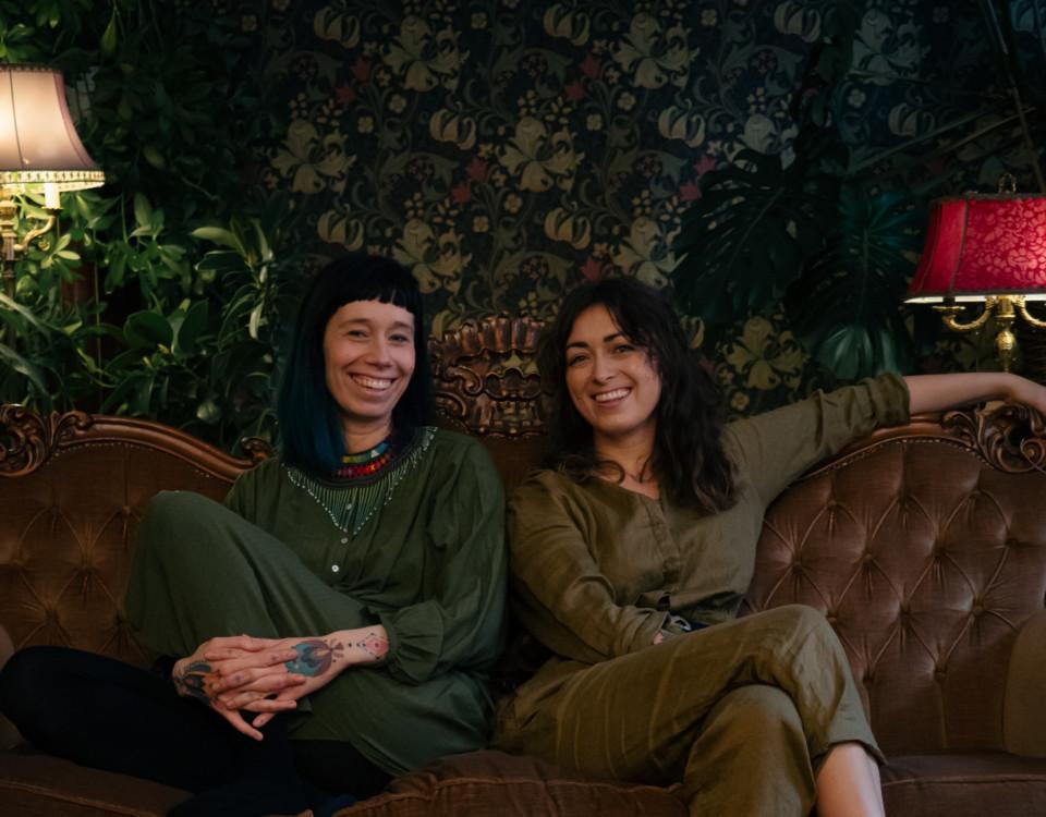 Två leende kvinnor sitter i en soffa