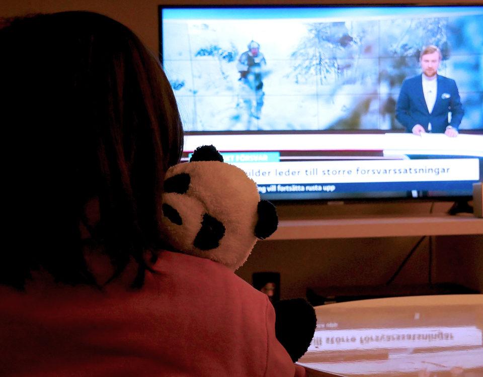 Ett barn med ett mjukisdjur i famnen sitter framför en påslagen tv
