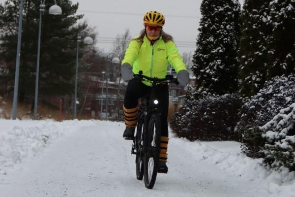 En kvinna som komemr cyklande i ett vintrigt landskap.