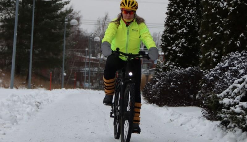 En kvinna som komemr cyklande i ett vintrigt landskap.